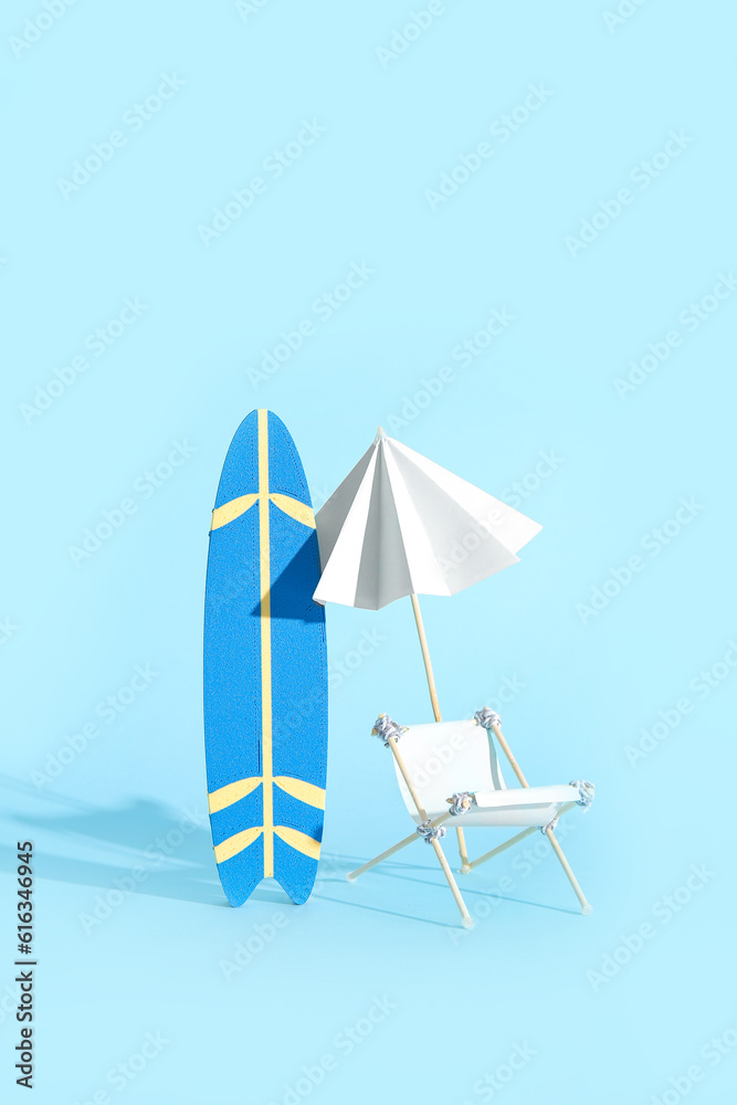 Creative composition with miniature surfboard, deckchair and umbrella on blue background