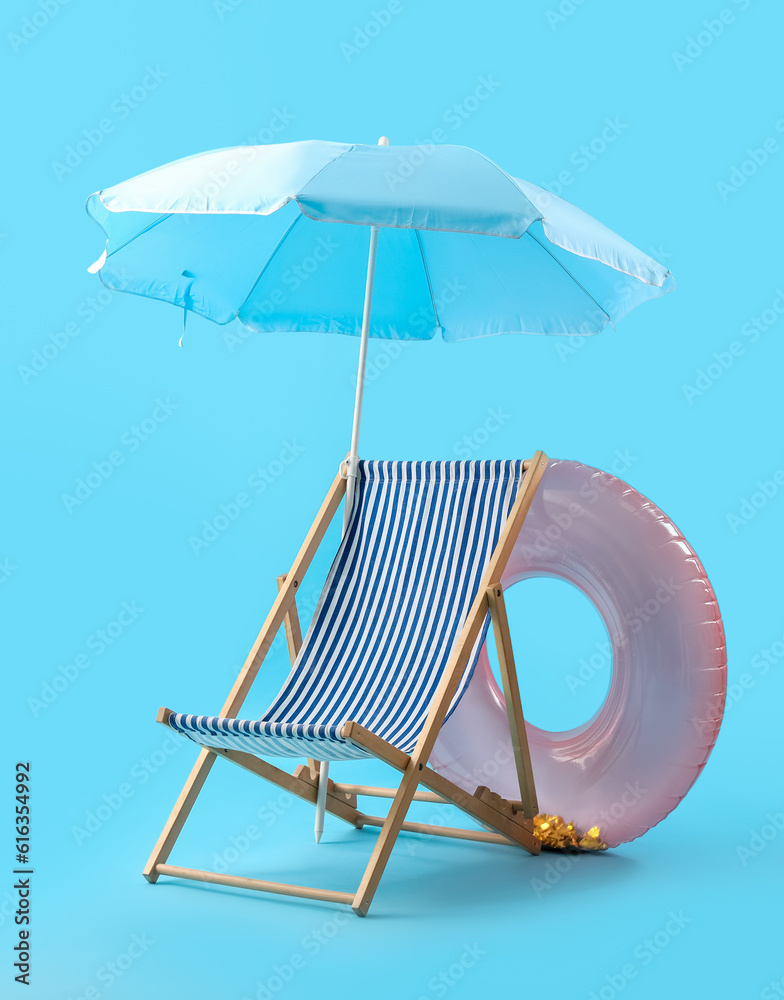 Deckchair with umbrella and inflatable ring on blue background. Summer vacation concept