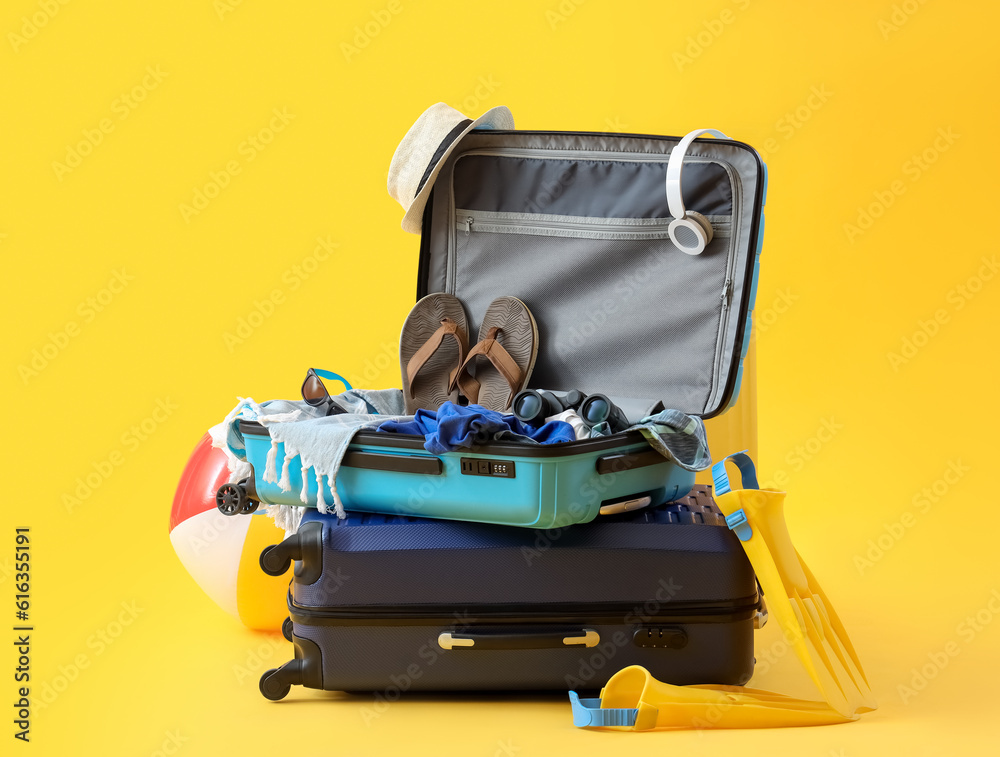 Suitcases with inflatable ball, beach accessories and headphones on yellow background. Summer vacati