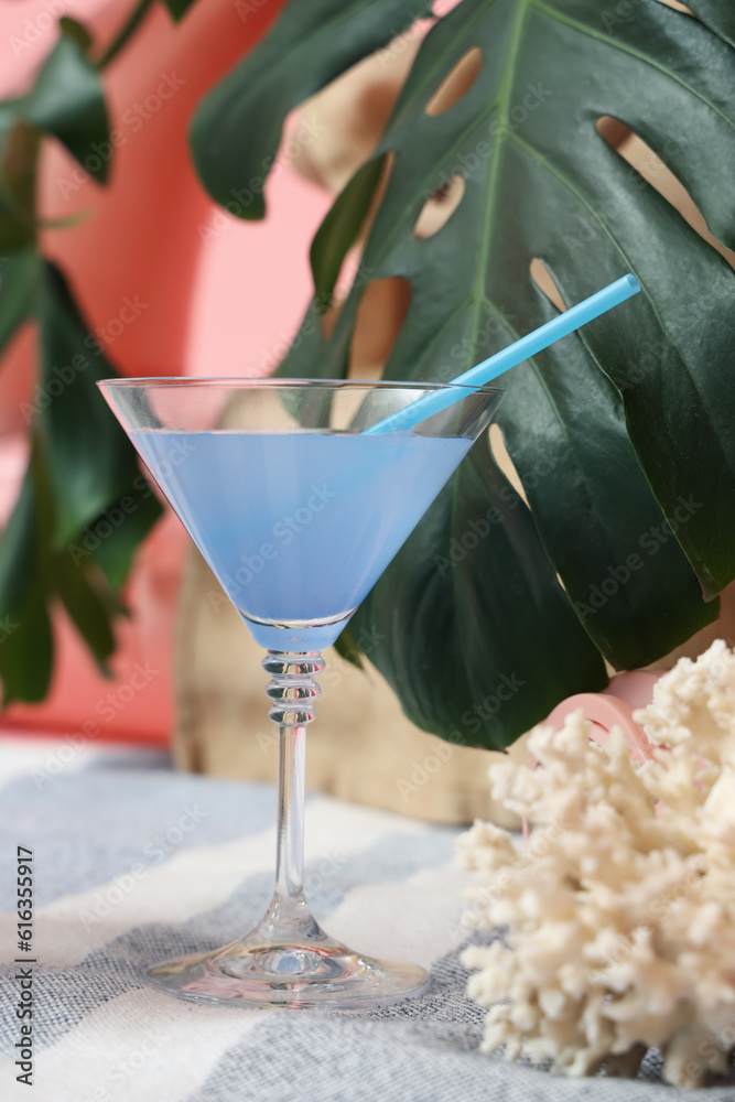 Cocktail with palm leaves and coral on beach blanket against pink background. Travel concept