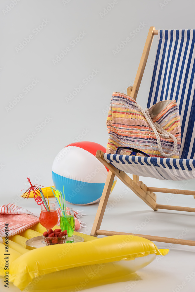 Deckchair with beach accessories, cocktails and bowl of strawberry on grey background. Travel concep