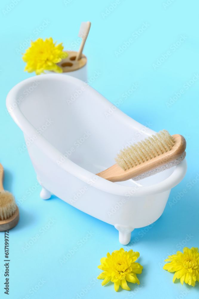 Small bathtub , massage brushes and flowers on color background