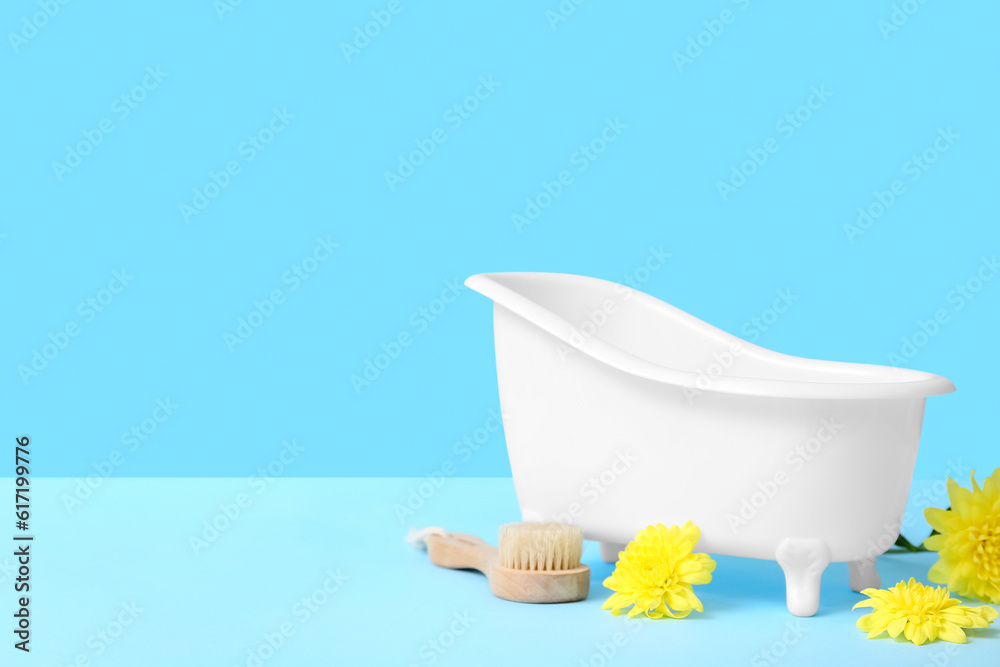 Small bathtub, massage brush and flowers on color background