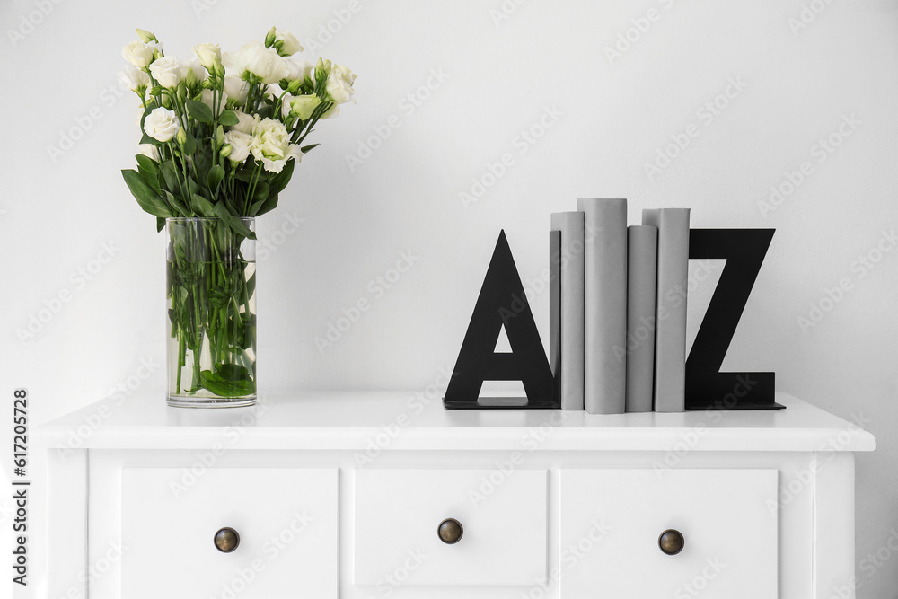 Bookend and vase with roses on table near light wall