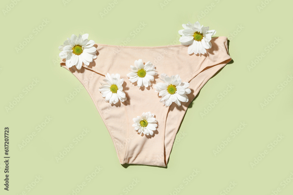 Composition with female panties and beautiful chamomile flowers on green background