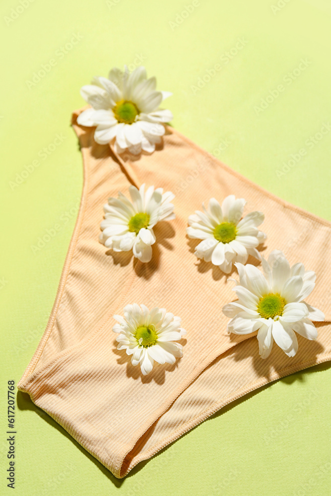 Composition with female panties and beautiful chamomile flowers on green background, closeup