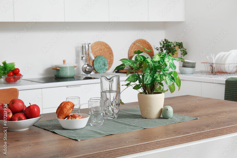 Wooden island table with houseplant, apples and cinnamon rolls in modern kitchen