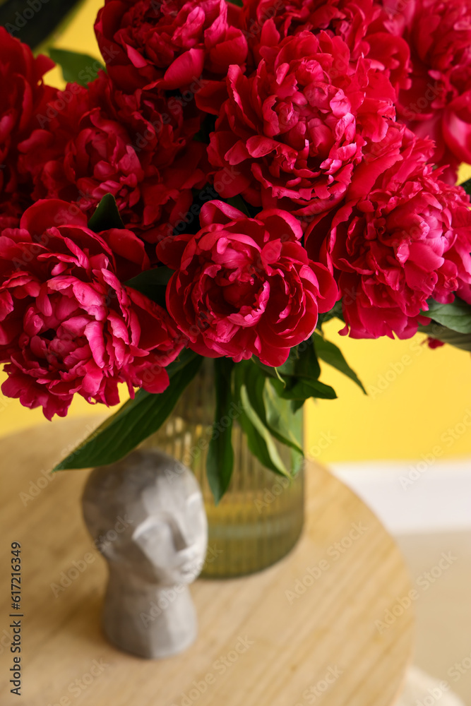 Vase of red peonies with figurine near yellow wall