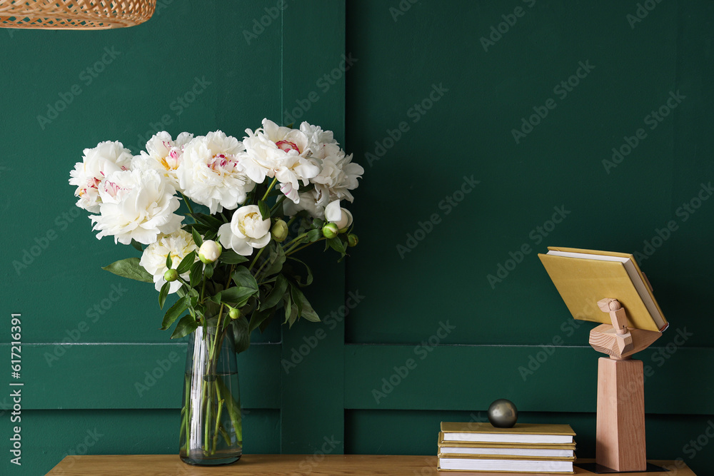 Vase of white peonies with books on dresser near green wall