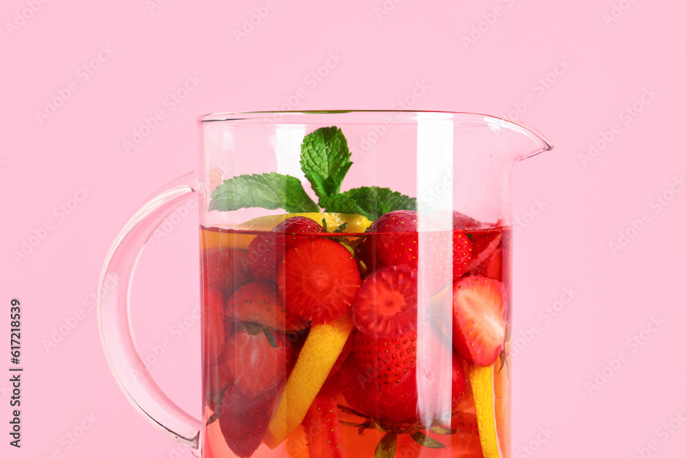 Jug of infused water with strawberry and lemon on pink background
