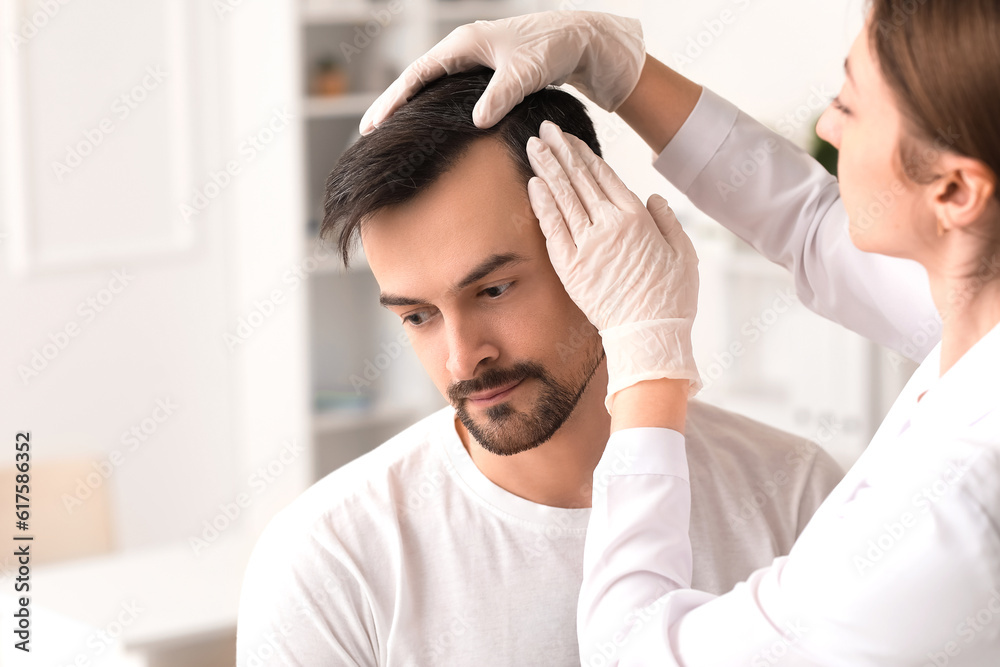 Doctor examining young mans hair in clinic, closeup