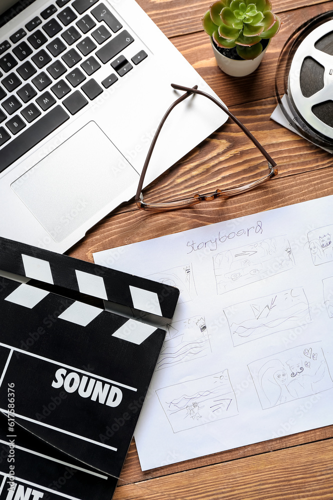 Storyboard with movie clapper, laptop and eyeglasses on wooden background
