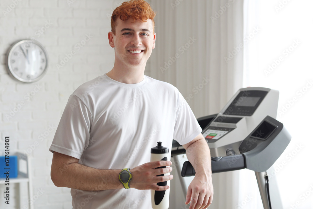 Young redhead man with sports water bottle in gym
