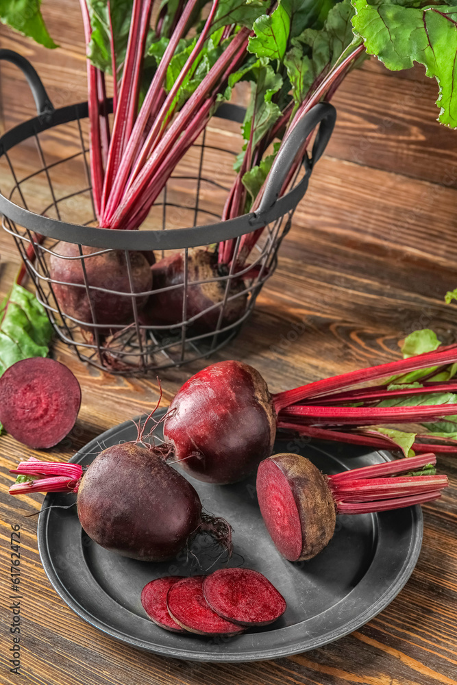 Plate and basket of fresh beets with green leaves on wooden background
