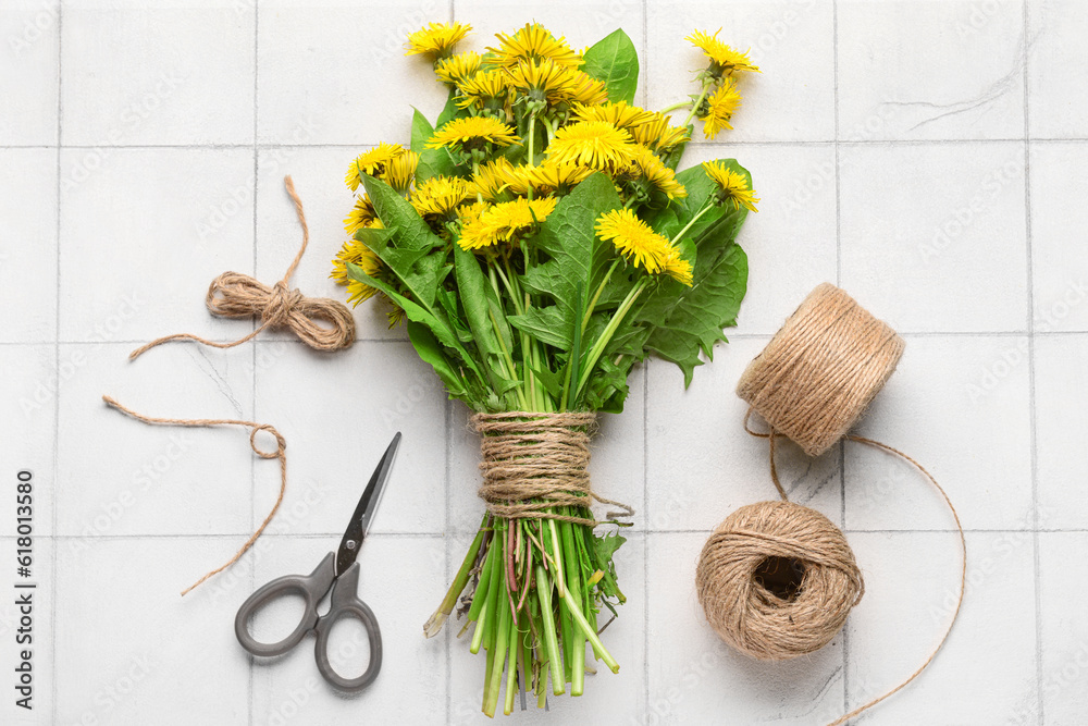 Bouquet of beautiful dandelion flowers, rope and scissors on light tile background