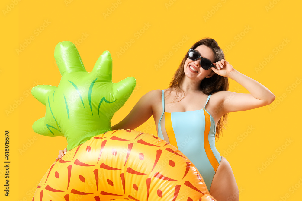 Young woman with swim ring in shape of pineapple on yellow background