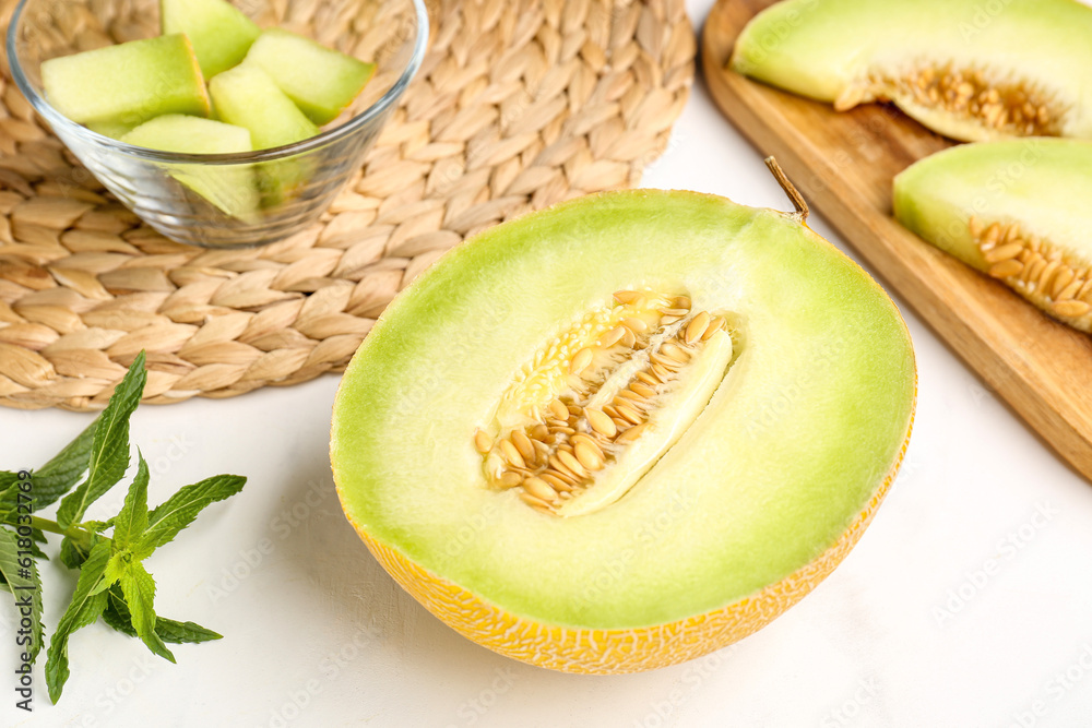 Half of sweet melon and wooden board with pieces on white background