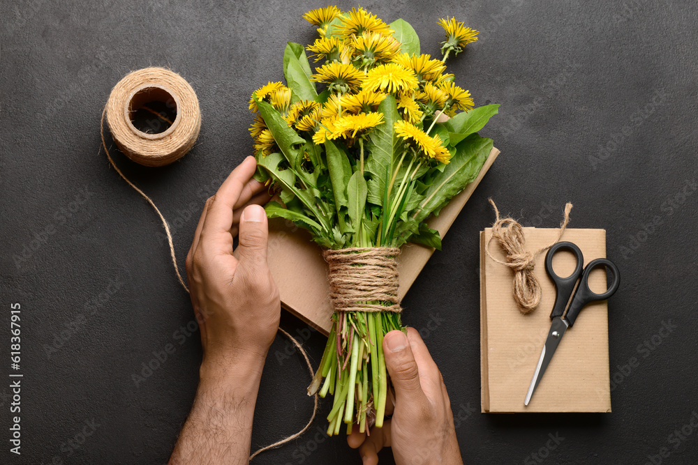 Male hands with bouquet of beautiful dandelion flowers, rope, scissors and books on dark background,
