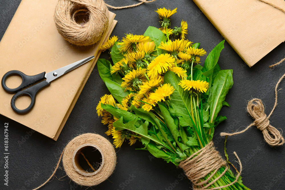 Bouquet of beautiful dandelion flowers, rope, scissors and books on dark background, closeup