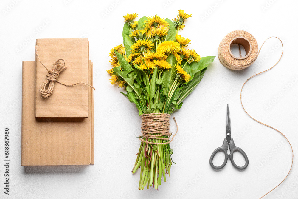 Bouquet of beautiful dandelion flowers, rope, scissors and books on light background