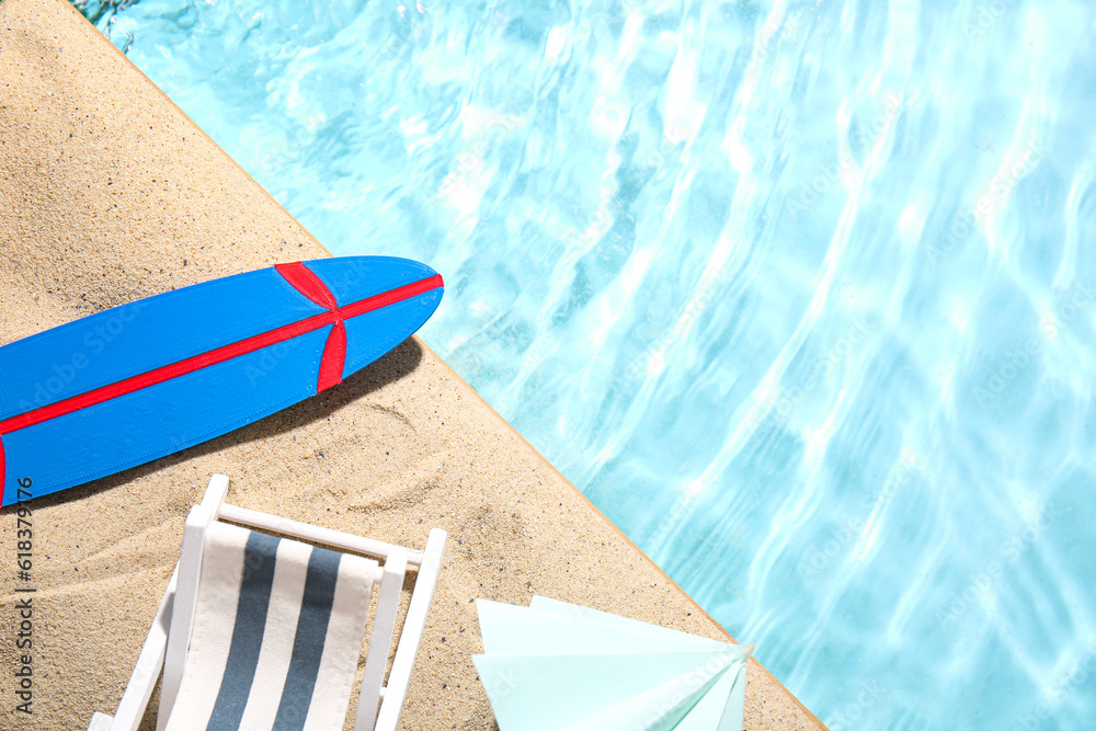Mini surfboard with deckchair and umbrella on sand near water