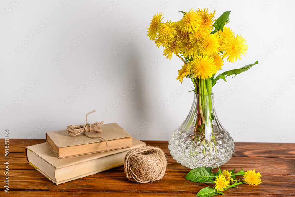 Vase with beautiful dandelion flowers, rope and books on wooden table near light wall
