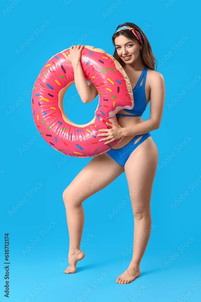 Young woman with swim ring in shape of doughnut on blue background