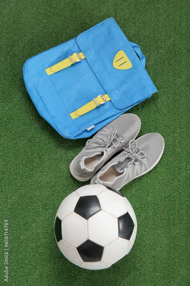 Sneakers with backpack and soccer ball on color background