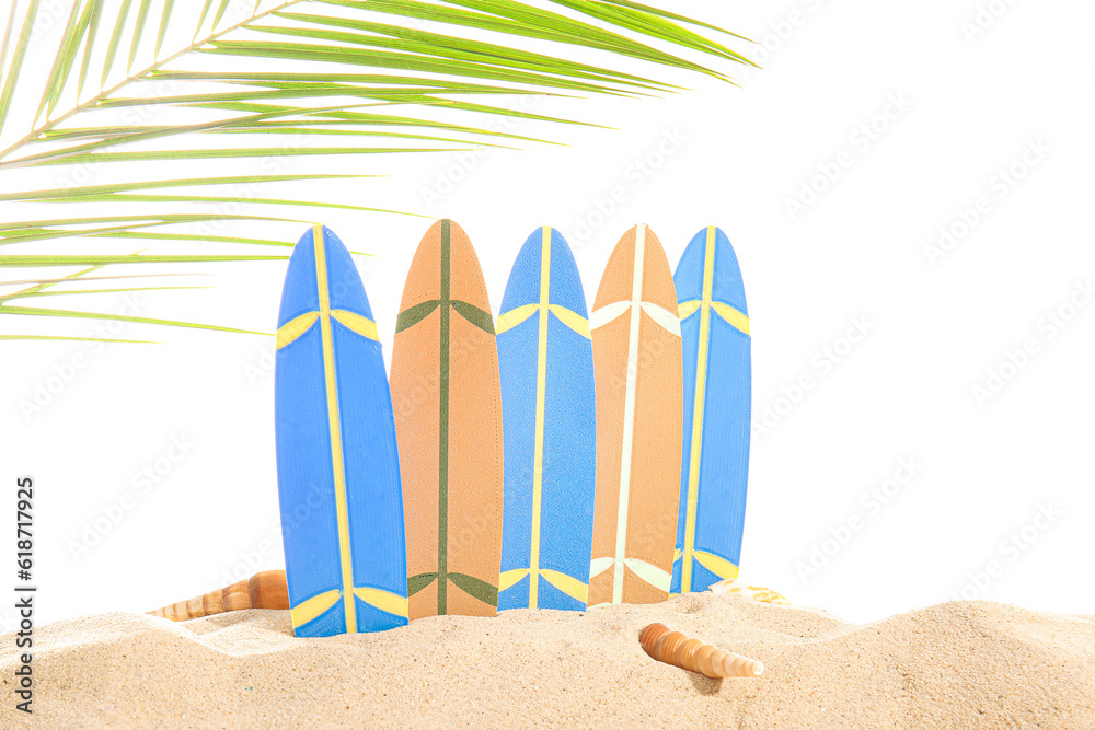 Mini surfboards with seashells and palm leaf on sand against white background