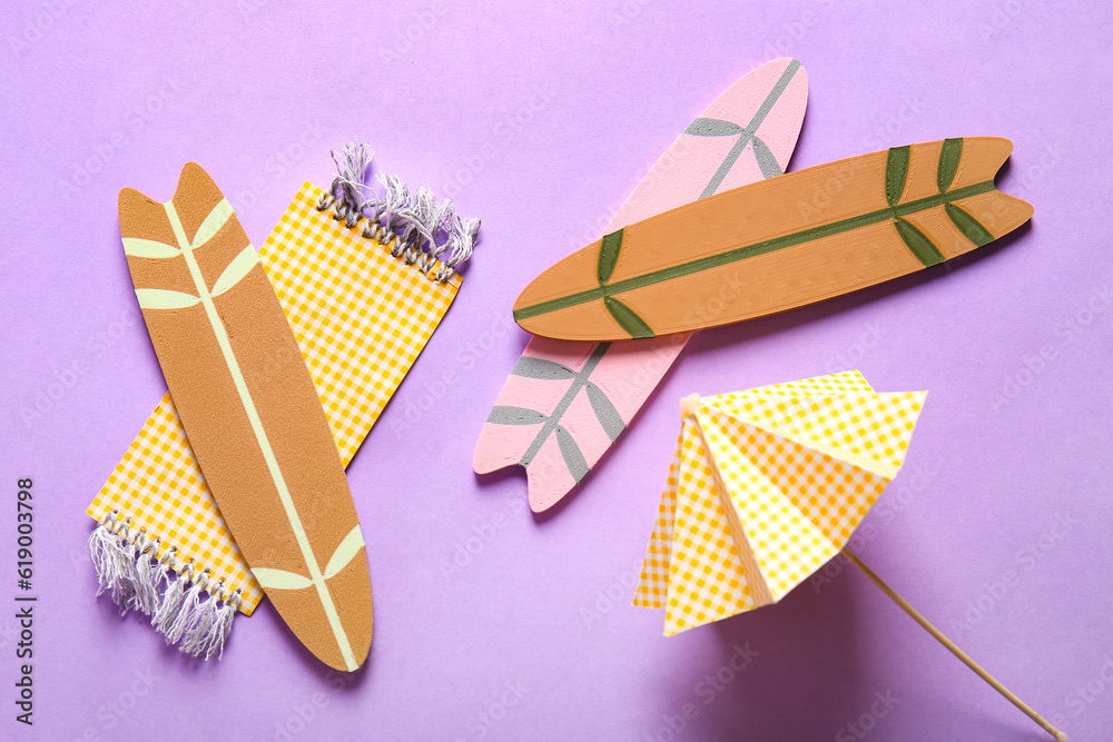 Creative summer composition with mini surfboards, umbrella and beach blanket on purple background