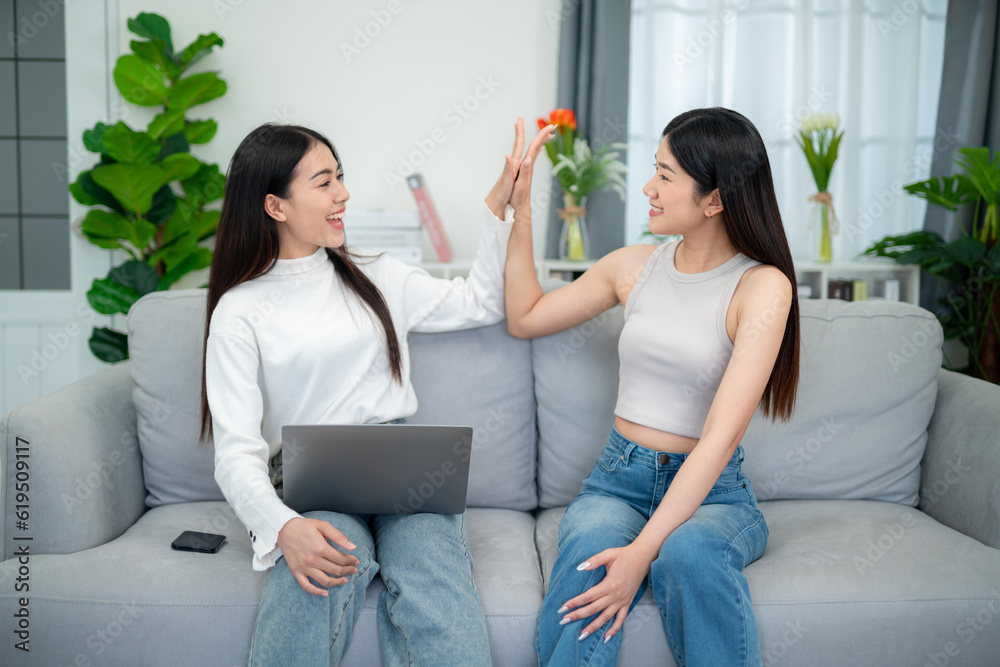 Two asian young women showing success together on sofa with laptop in living room. The concept of tr