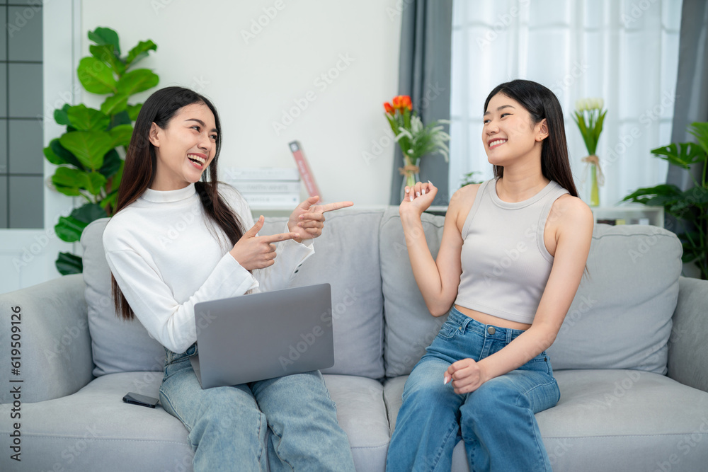 Two asian young women having fun together while sitting on the sofa in the living room.