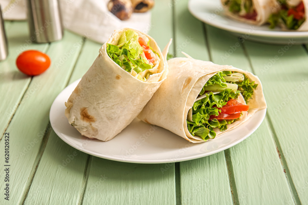 Plate of tasty lavash rolls with tomatoes and greens on green wooden background