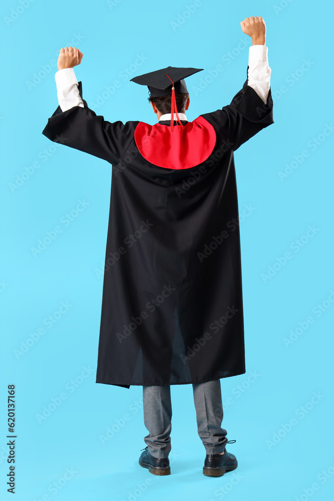 Happy male graduate student on blue background, back view