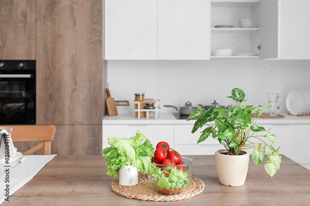 Wooden island table with fresh vegetables and houseplant in modern kitchen