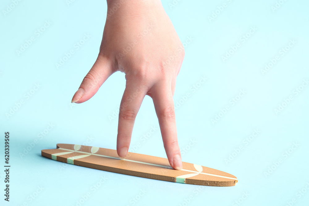 Creative composition with mini surfboard and female hand on blue background
