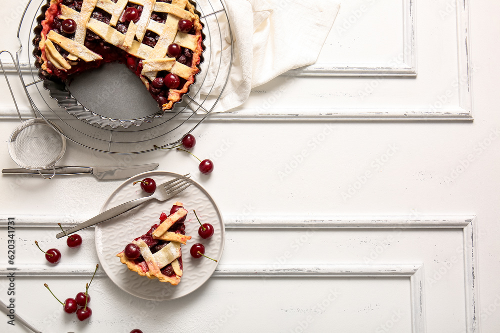 Baking dish with tasty cherry pie and plate of piece on white background