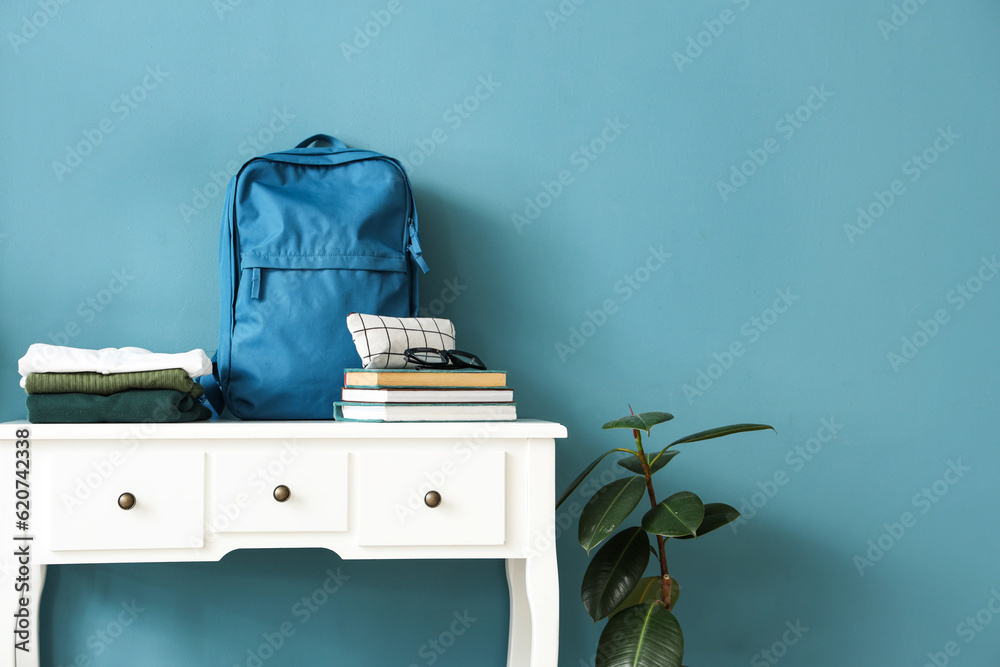 Table with stack of stylish school uniform, backpack, books, eyeglasses and pencil case near blue wa