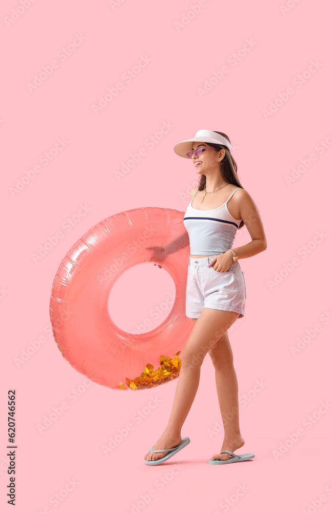 Young woman with inflatable ring on pink background