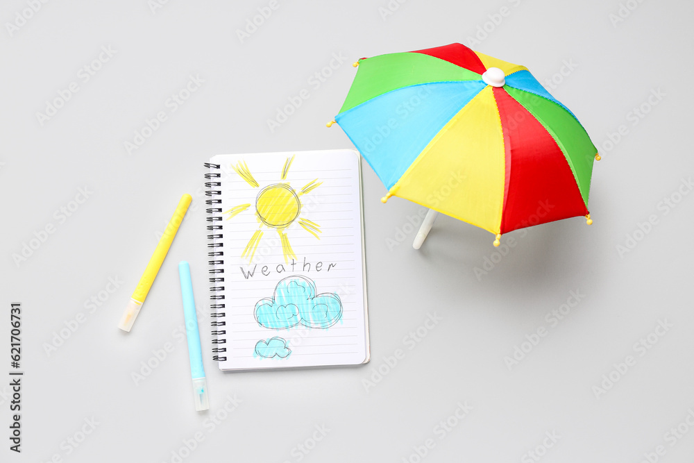Notebook with word WEATHER, drawings and umbrella on light background