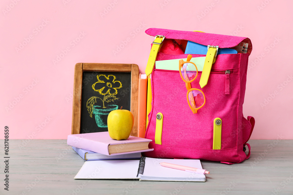 Pink school backpack with books, chalk drawing flower and apple on grey wooden table near color wall