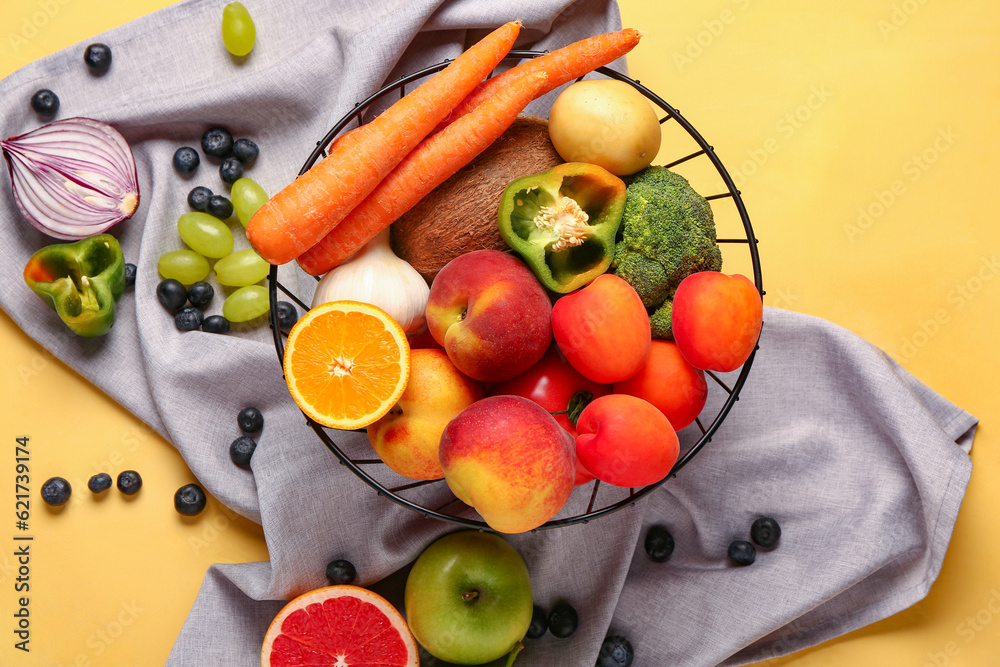 Basket with different fresh fruits and vegetables on yellow background