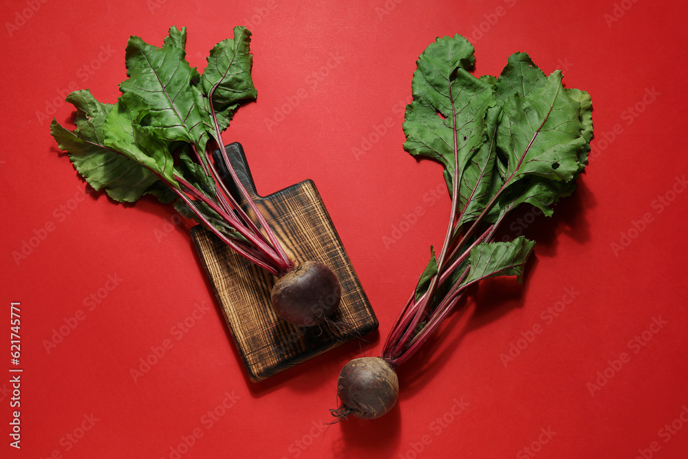 Cutting board with fresh beetroots on red background