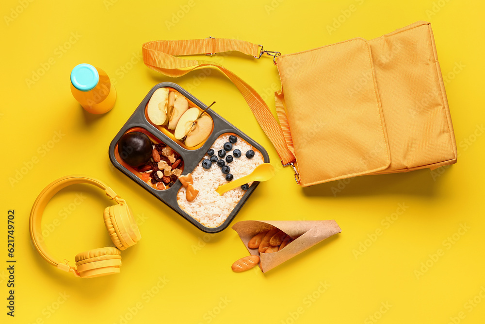 Backpack, headphones and lunchbox with tasty food on yellow background