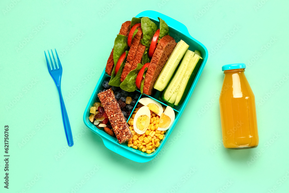 Bottle of juice, fork and lunchbox with tasty food on turquoise background