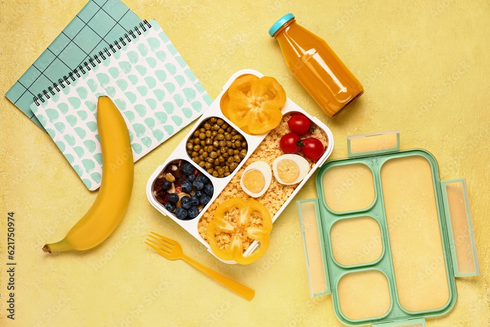Bottle of juice, notebooks and lunchbox with tasty food on yellow background