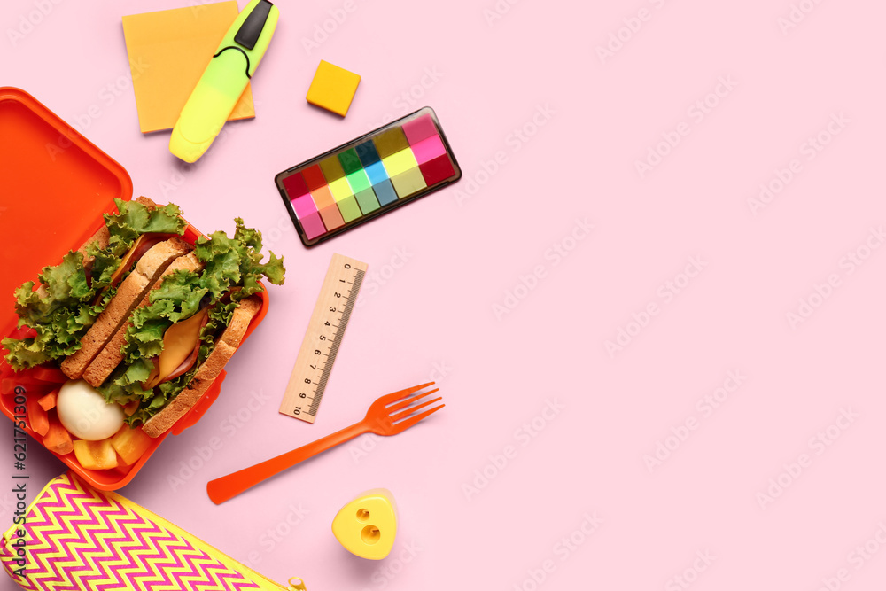Stationery and lunchbox with tasty food on pink background