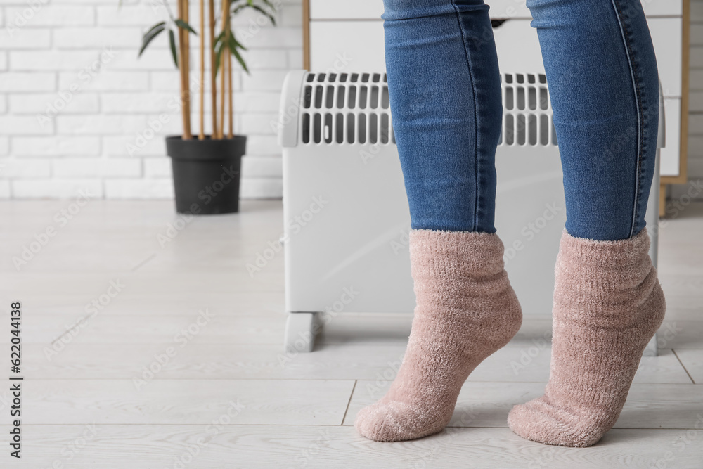 Woman in warm socks near radiator at home, closeup