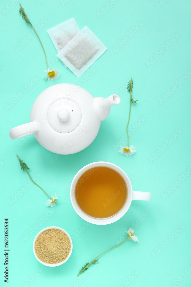 Teapot and cup of hot chamomile tea with honey on turquoise background