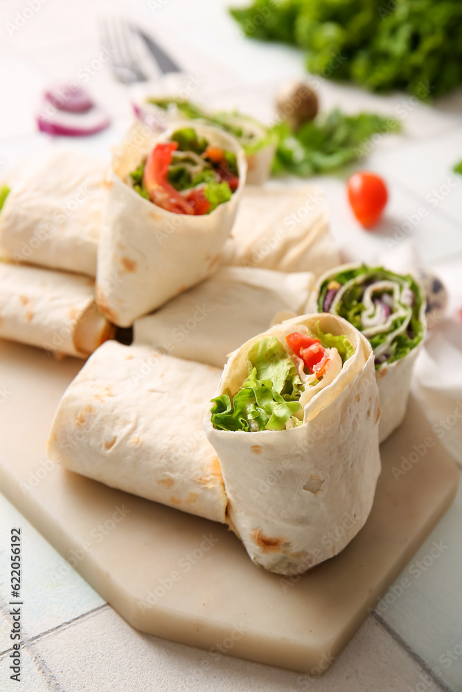 Board of tasty lavash rolls with vegetables on white tile background